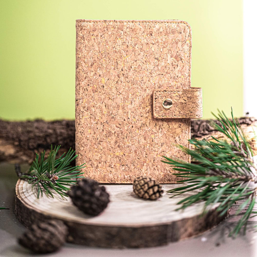 Cork notebook with a strap on a wooden surface with pine cones and branches.