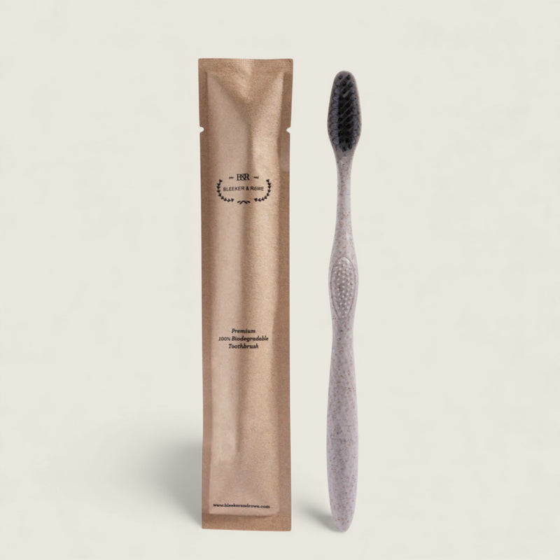 Gray toothbrush with black bristles next to its packaging on a beige background
